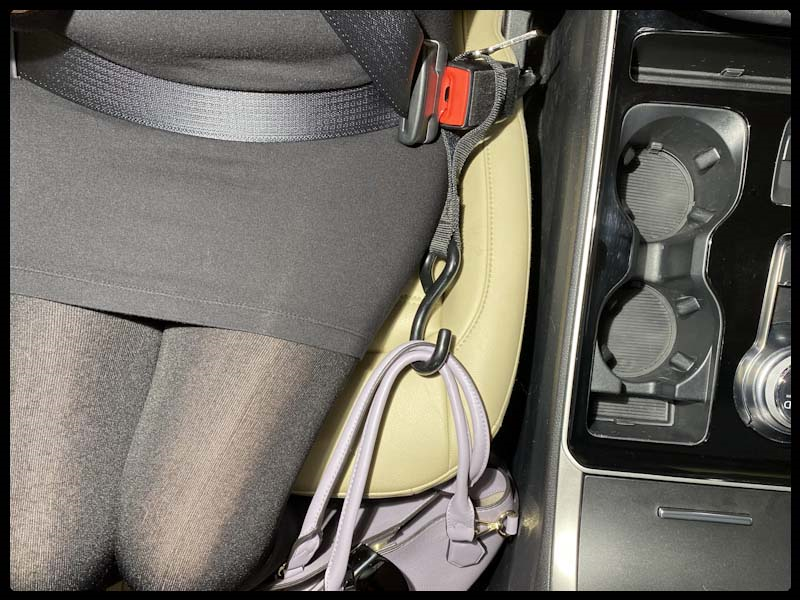 Woman in automobile passenger seat using Hook & Go to secure her pink purse beside her while safely buckled into the seat belt