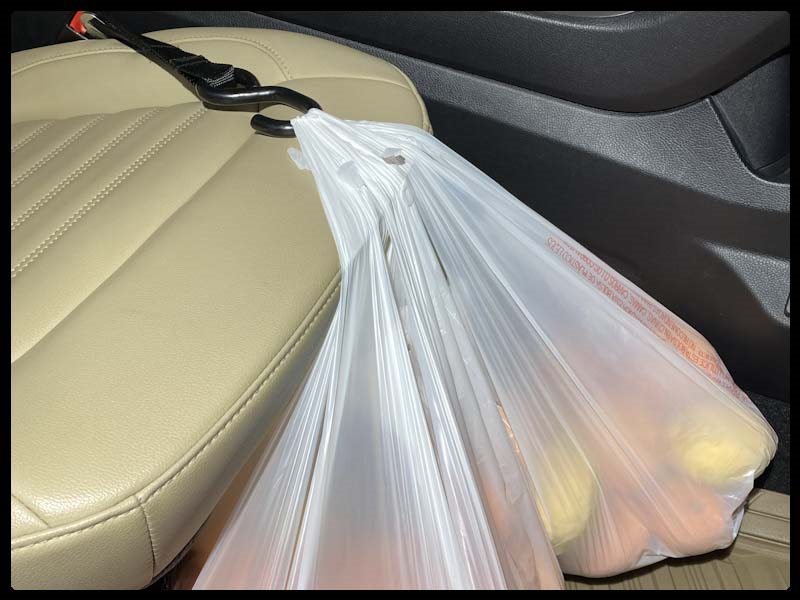 White shopping bags suspended over seat, secured by a Hook & Go inserted into the front passenger seat belt buckle