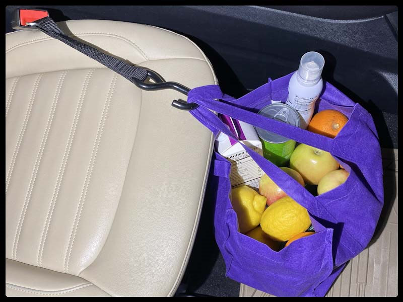 Purple shopping bag suspended over seat, secured by a Hook & Go inserted into the front passenger seat belt buckle