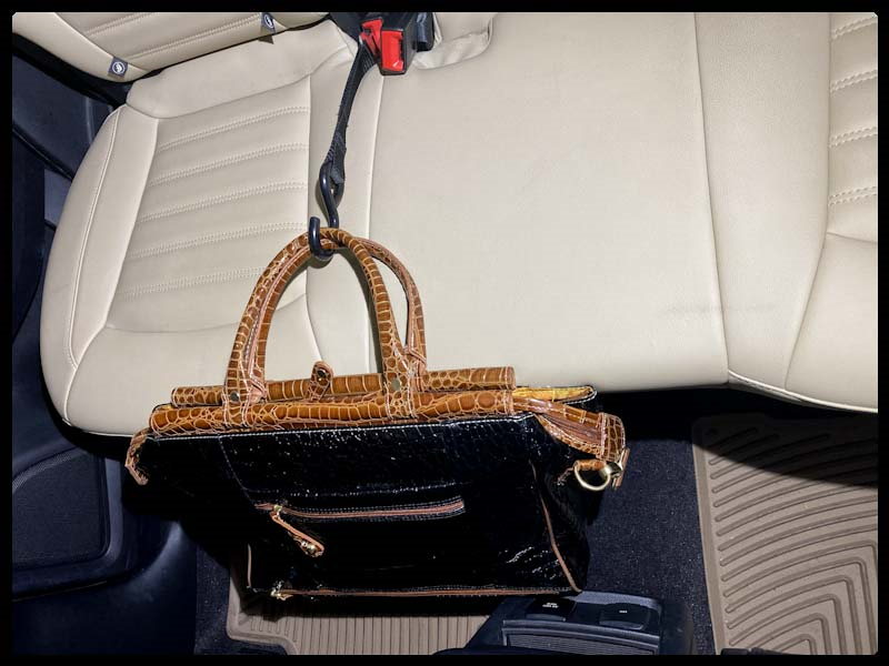 Fancy black handbag suspended over seat, secured by a Hook & Go inserted into the front passenger seat belt buckle