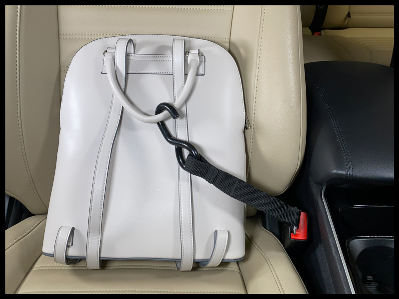 White backpack purse on seat secured by a Hook & Go inserted into the front passenger seat belt buckle